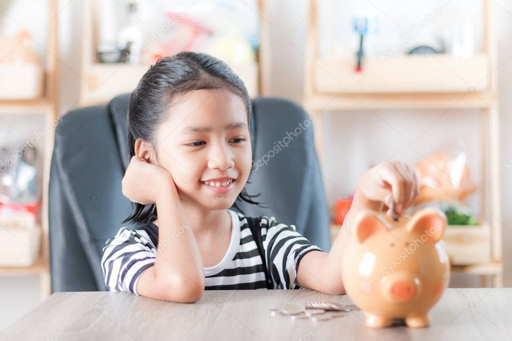 Asian little girl in putting coin in to piggy bank shallow depth of field select focus at the face