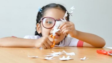 Asyalı küçük kız Tay anaokulu öğrencisi üniformalı aile şekil baba anne oğul ve eller odaklanmak seçin kızı ahşap masa üzerine beyaz kağıt kesmek için makas kullanarak