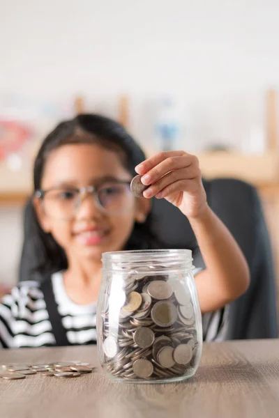 Азиатская маленькая девочка в положить монету в стеклянную банку мелкой глубины — стоковое фото
