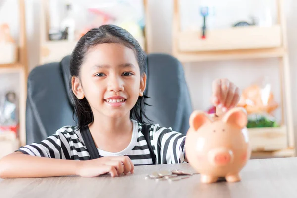 Asiática niña en poner moneda en a alcancía superficial profundidad — Foto de Stock