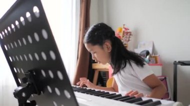 Asyalı küçük kız evde eğitim acemi müzik enstrümantal kendini için elektrikli synthesizer klavye kullanarak temel piyano çalmayı öğrenme