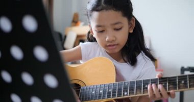 Asyalı küçük kız evde eğitim acemi müzik enstrümantal kendini için akustik gitar kullanarak temel gitar çalmayı öğrenme