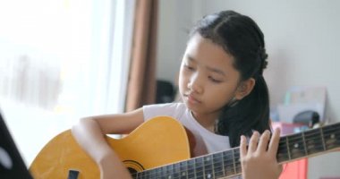 Asyalı küçük kız evde eğitim acemi müzik enstrümantal kendini için akustik gitar kullanarak temel gitar çalmayı öğrenme