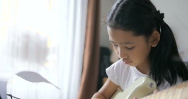 Asyalı küçük kız evde eğitim acemi müzik enstrümantal kendini için elektrik gitar kullanarak temel gitar çalmayı öğrenme