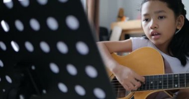 Asyalı küçük kız evde eğitim acemi müzik enstrümantal kendini için akustik gitar kullanarak temel gitar çalmayı öğrenme