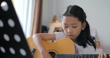 Asyalı küçük kız evde eğitim acemi müzik enstrümantal kendini için akustik gitar kullanarak temel gitar çalmayı öğrenme