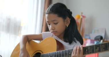 Asyalı küçük kız evde eğitim acemi müzik enstrümantal kendini için akustik gitar kullanarak temel gitar çalmayı öğrenme