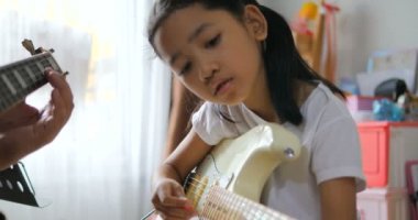 Asyalı küçük kız evde eğitim acemi müzik enstrümantal kendini için elektrik gitar kullanarak temel gitar çalmayı öğrenme