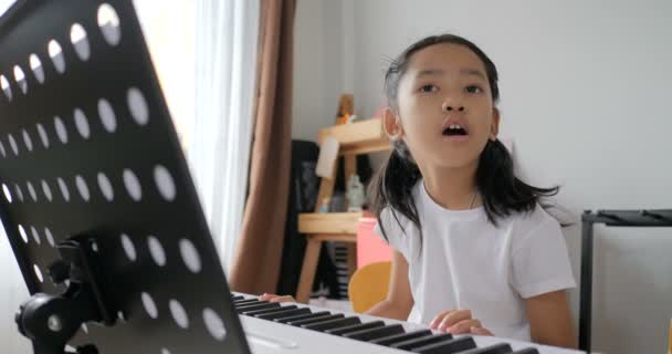 初心者の音楽楽器の自己学習のための電気シンセサイザーキーボードを使用して基本的なピアノを演奏することを学ぶアジアの小さな女の子 — ストック動画