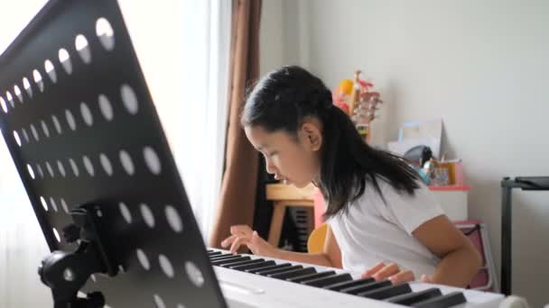 初心者の音楽楽器の自己学習のための電気シンセサイザーキーボードを使用して基本的なピアノを演奏することを学ぶアジアの小さな女の子 — ストック動画