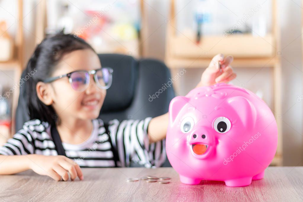 Asian little girl in putting coin in to piggy bank shallow depth