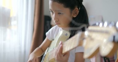 Asyalı küçük kız evde eğitim acemi müzik enstrümantal kendini için elektrik gitar kullanarak temel gitar çalmayı öğrenme