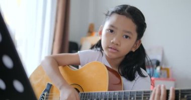 Asyalı küçük kız evde eğitim acemi müzik enstrümantal kendini için akustik gitar kullanarak temel gitar çalmayı öğrenme