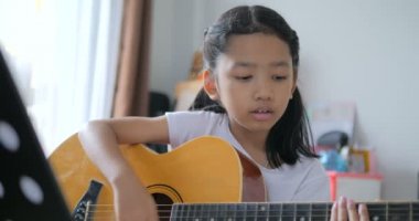 Asyalı küçük kız evde eğitim acemi müzik enstrümantal kendini için akustik gitar kullanarak temel gitar çalmayı öğrenme