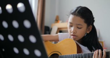 Asyalı küçük kız evde eğitim acemi müzik enstrümantal kendini için akustik gitar kullanarak temel gitar çalmayı öğrenme