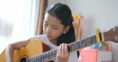Asyalı küçük kız evde eğitim acemi müzik enstrümantal kendini için akustik gitar kullanarak temel gitar çalmayı öğrenme