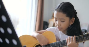 Asyalı küçük kız evde eğitim acemi müzik enstrümantal kendini için akustik gitar kullanarak temel gitar çalmayı öğrenme