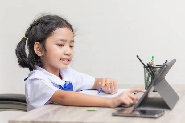 Aziatische meisje in student uniform huiswerk doen en met behulp van ta — Stockfoto