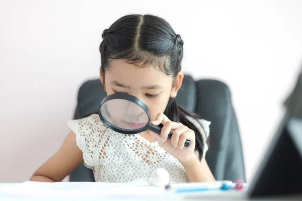 Kleine asiatische Mädchen mit Lupe tun Hausaufgaben für Bildung c — Stockfoto