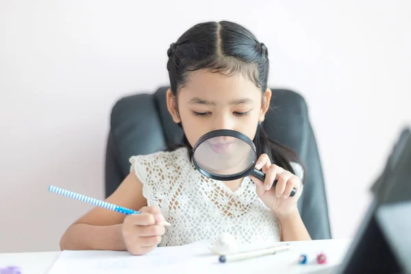 Pequeña chica asiática usando lupa haciendo tarea para la educación c —  Fotos de Stock