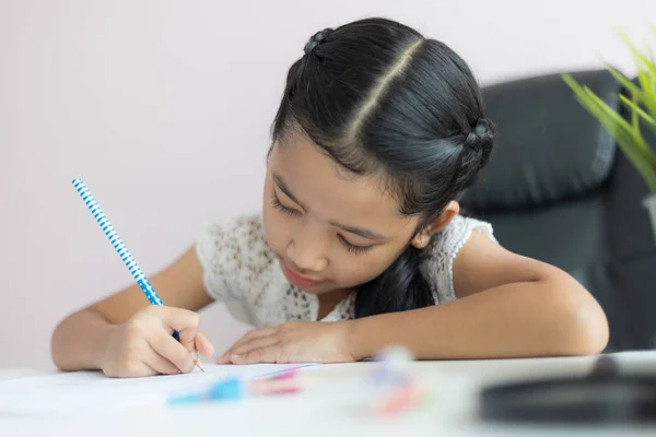 Liten asiatisk tjej som använder pennan för att skriva på papperet gör h — Stockfoto