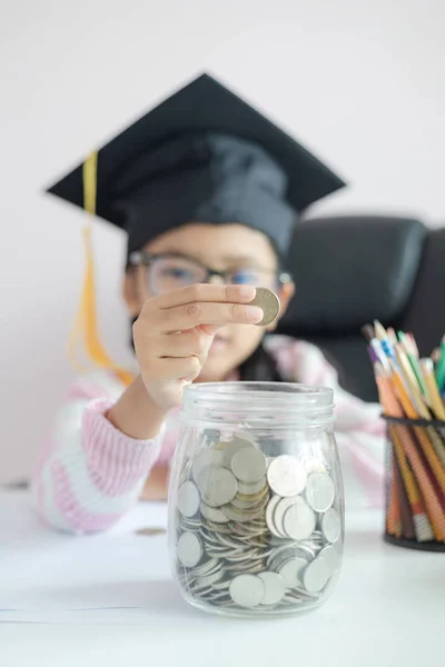 Pequeña chica asiática con sombrero de graduado poner la moneda en el círculo — Foto de Stock