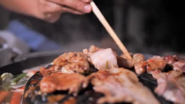 人们用筷子做饭 拿起和翻转猪肉 在火锅上与黑暗和谷物加工的韩国 Bbq — 图库视频影像