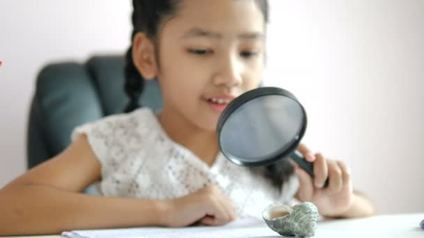 Kleine Asiatische Mädchen Mit Lupe Hausaufgaben Machen Und Lächeln Vor — Stockvideo