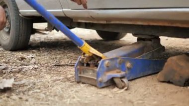 Lades kemiği kontrol kolunu onarmak ve arabanın ön tekerleğini değiştirmek için kamyonu kaldırmak için araba kalıbını kullanan tamirci