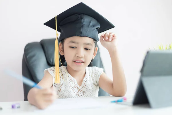 Trochę Asian Dziewczyna noszenie absolwent kapelusz robi pracę domową i uśmiech — Zdjęcie stockowe