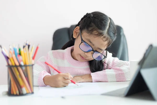 Liten asiatisk tjej som använder pennan för att skriva på papperet gör h — Stockfoto