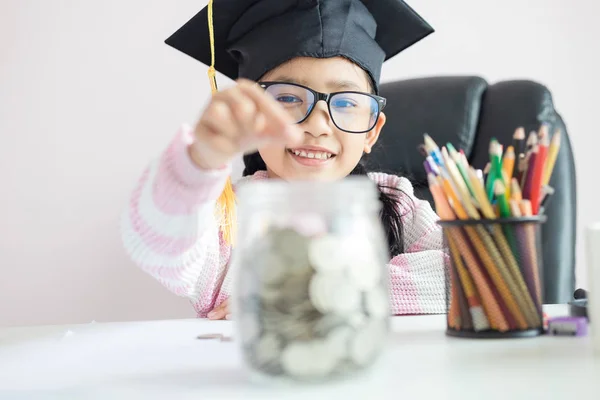 Pequeña chica asiática con sombrero de graduado poner la moneda en el círculo — Foto de Stock