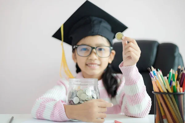 Pequeña chica asiática con sombrero de graduado poner la moneda en el círculo — Foto de Stock