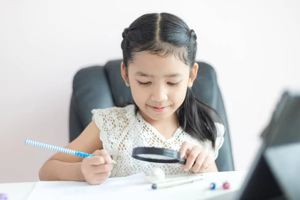 Pequeña chica asiática usando lupa haciendo tarea y sonrisa con —  Fotos de Stock