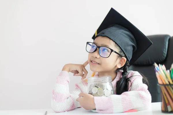 Pequeña chica asiática con sombrero de graduado abrazando tarro de vidrio claro p — Foto de Stock
