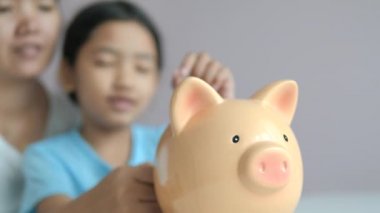 Anne ve küçük Asyalı kız daha iyi bir gelecek için para tasarrufu kumbara metafor içine sikke koyarak alan odak sığ derinlik seçin