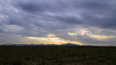 Zaman atlamalı manzara bulutu kuru bir tarladan geçerek dağ ve gökyüzüne doğru ilerliyor, günbatımı atmosferinde, karanlık ve tahıl işlenmiş.