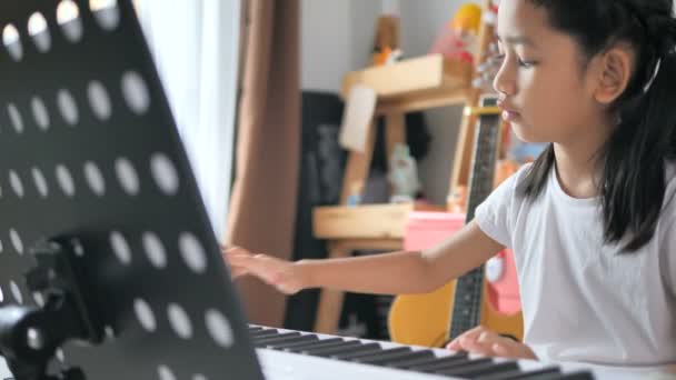 아시아인작은 소녀는 가정에서의 음악의 학습을 신시사이저 키보드를 사용하여 피아노 연주를 — 비디오