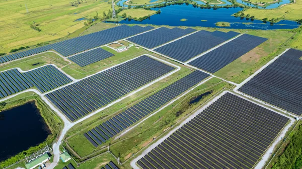 Drone 'un hava görüntüsü güneş enerjisi dizisi kırsal alanda yeşil ve suyla çevrili büyük ölçekli bir tesiste yenilenebilir enerji sağlıyor. Kırsaldaki güneş çiftliği