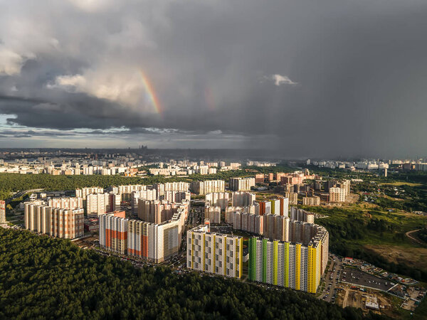 High-rise buildings near the forest under the sky with a rainbow