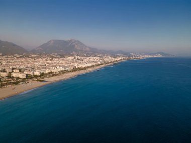Deniz ve güzel sahil, arkasında dağlar ve küçük bir kasaba var.