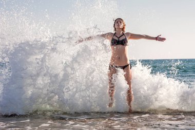 Kız deniz dalgasının spreyinde duruyor.