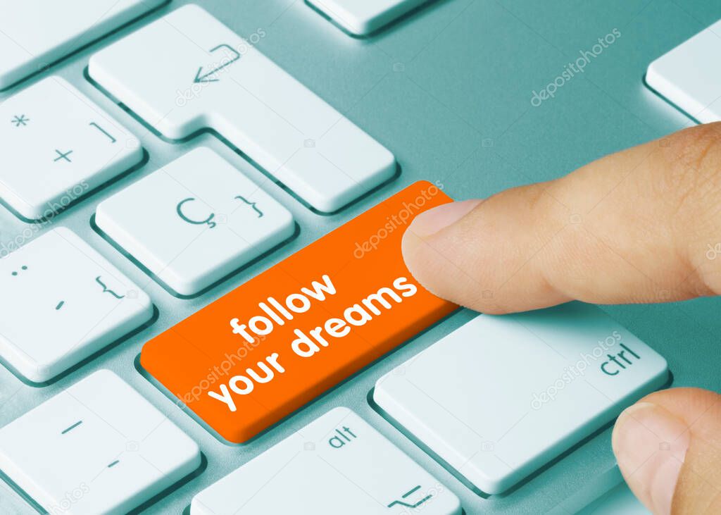follow your dreams Written on Orange Key of Metallic Keyboard. Finger pressing key.