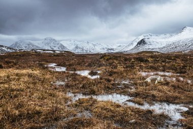 Fırtınalı gökyüzü ile İskoçya kışı manzarası. Kara Dağ 'ın karlı zirveleri Rannoch Moor' un lochans boyunca uzanır..