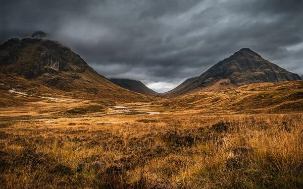 Glen Coe, İskoçya 'da sonbahar manzarası. Buachaille Etive Beag ve Aonach Eagach tepelerinde kara bulutlar sallanıyor..