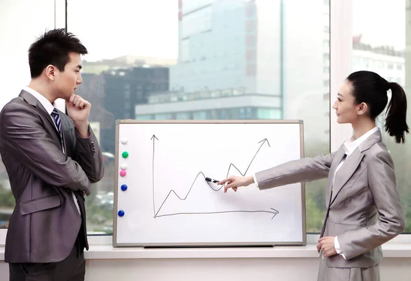 Businessman and businesswoman standing in front of line graph,pointing to line