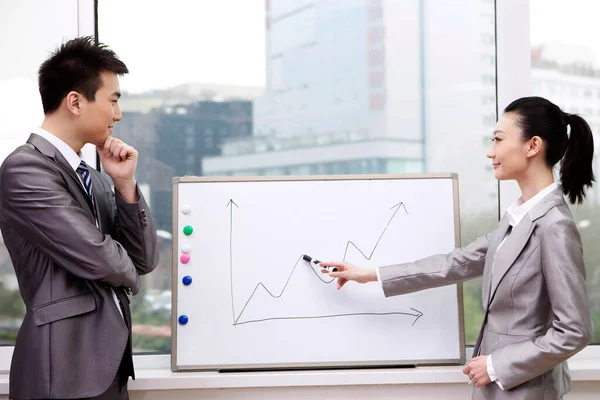 Businessman and businesswoman standing in front of line graph, pointing to line