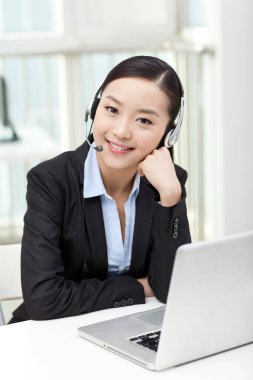 Dizüstü bilgisayar kullanan ve kulaklık takan genç bir kadın.