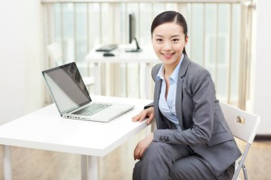 Genç bir kadın dizüstü bilgisayarın önünde oturuyor.