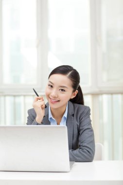 Genç bir kadın dizüstü bilgisayarın önünde oturuyor.